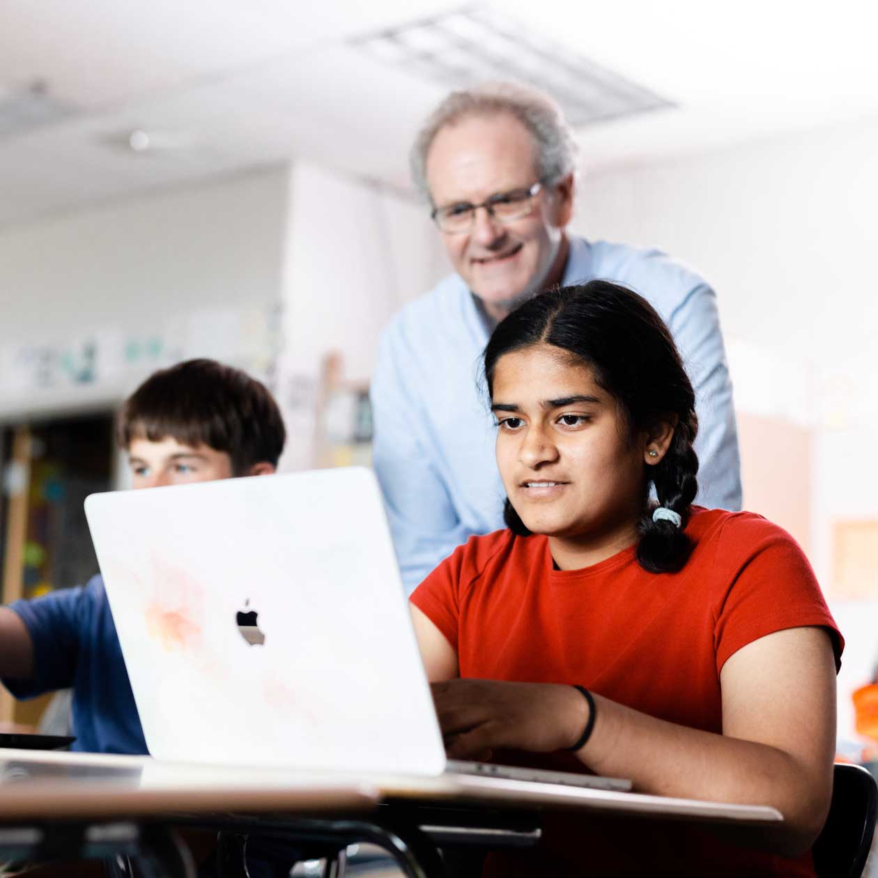 A professor standing next to a student using a laptop